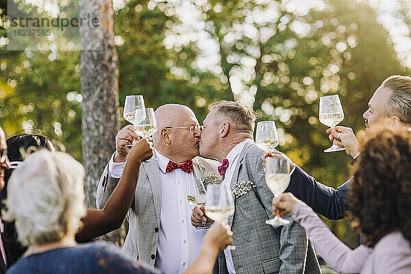 Neuvermähltes schwules Paar küsst sich  während es inmitten der Gäste einen Toast ausspricht