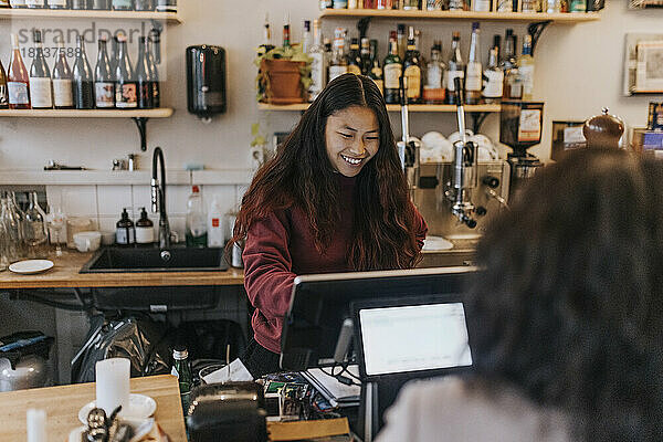 Lächelnde junge Besitzerin nimmt die Bestellung eines Kunden in einem Café entgegen