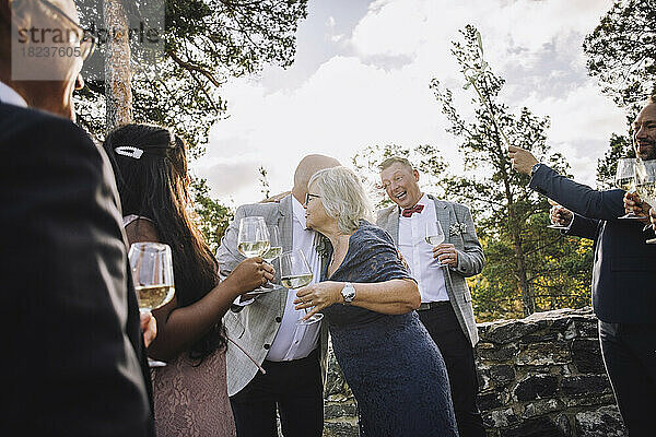 Ältere Frau umarmt Bräutigam mit Weingläsern inmitten der Hochzeitsgäste