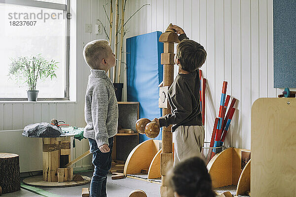 Junge stapelt Spielzeugblöcke  während ein männlicher Freund ihn in der Kindertagesstätte beobachtet