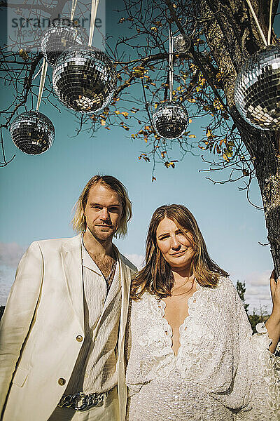 Porträt der neu verheirateten Mitte erwachsenen Bräutigam und Braut stehen unter Disco-Kugeln auf sonnigen Tag