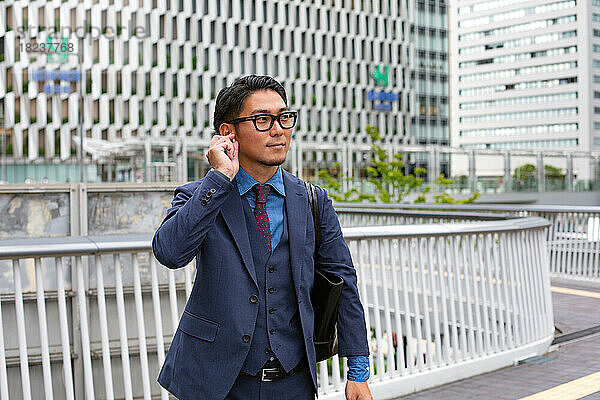 Ein junger Geschäftsmann in blauer Jacke  Hemd und Krawatte steht auf einem Gehweg in der Innenstadt.