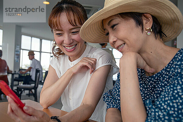 Zwei reife japanische Frauen  Freunde nebeneinander  sitzen und schauen auf den Bildschirm eines Mobiltelefons.