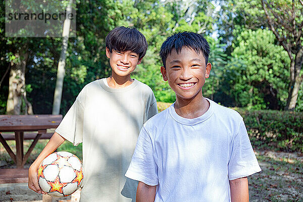 Zwei 13-jährige Jungen in einem Park mit einem Fußball im Sommer.