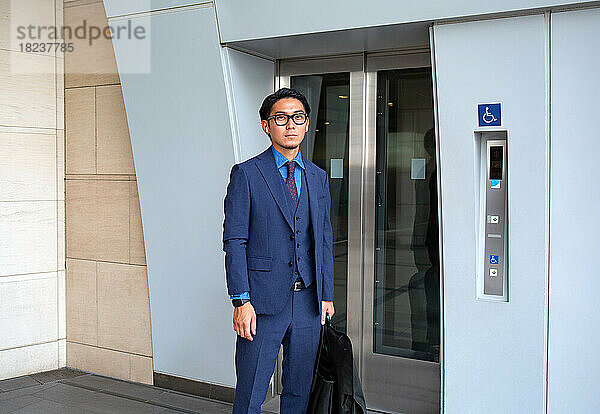 Ein junger Geschäftsmann in der Stadt  unterwegs  ein Mann steht an der Aufzugstür  mit Laptoptasche und Anzugträger.