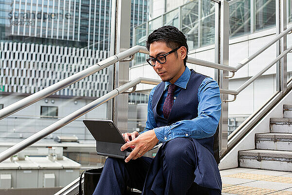 Ein junger Geschäftsmann in der Stadt  unterwegs  auf der Treppe am Fenster sitzend  einen Laptop benutzend.