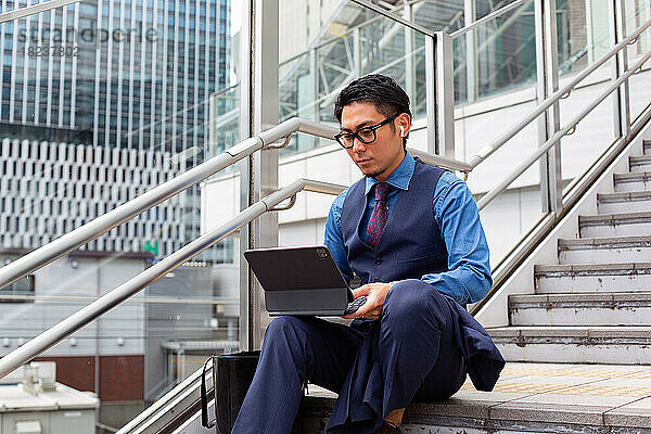 Ein junger Geschäftsmann in der Stadt  unterwegs  auf der Treppe am Fenster sitzend  einen Laptop benutzend.