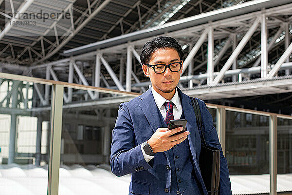 Ein junger Geschäftsmann in der Stadt  unterwegs  ein Mann im blauen Anzug mit Laptoptasche und einem Mobiltelefon in der Hand.