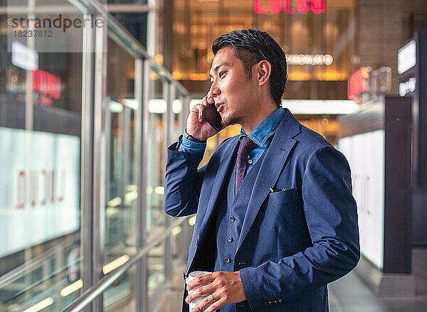 Ein junger Geschäftsmann im blauen Anzug ist in der Innenstadt unterwegs und spricht auf seinem Mobiltelefon.
