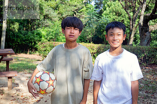 Zwei 13-jährige Jungen in einem Park mit einem Fußball im Sommer.