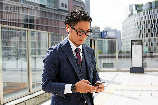 Ein junger Geschäftsmann in der Stadt  unterwegs  ein Mann draußen im Anzug  der auf sein Mobiltelefon schaut.