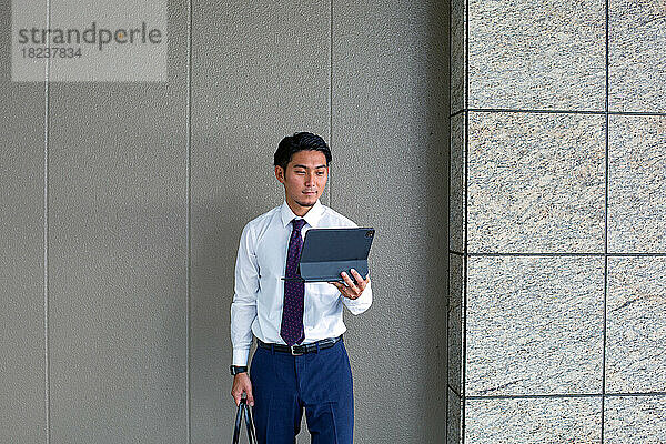 Ein junger Geschäftsmann in der Stadt  unterwegs  steht vor einem Gebäude und hält seinen Laptop in der Hand.