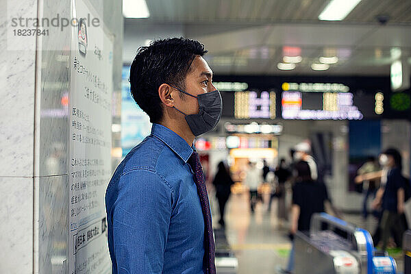 Ein junger Geschäftsmann in der Stadt  unterwegs  steht an einer U-Bahn-Station und trägt eine Gesichtsmaske.