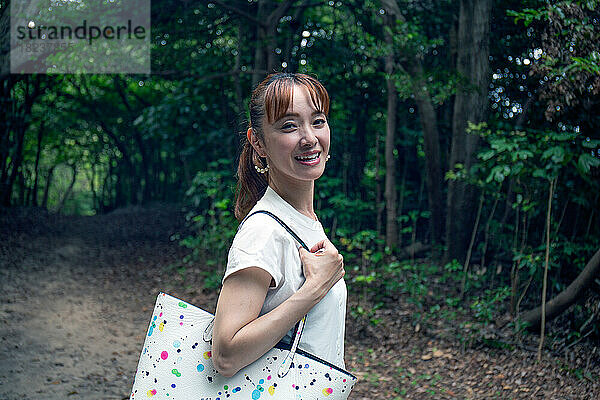 Eine reife Japanerin draußen in einem Park  den Kopf gedreht und lächelnd in die Kamera.
