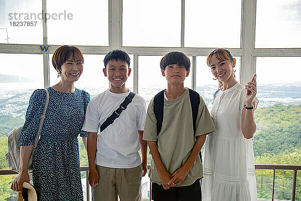 Vier Japaner  zwei Jungen und zwei reife Frauen  posieren bei einem Tagesausflug nebeneinander auf einer Aussichtsplattform für ein Foto.