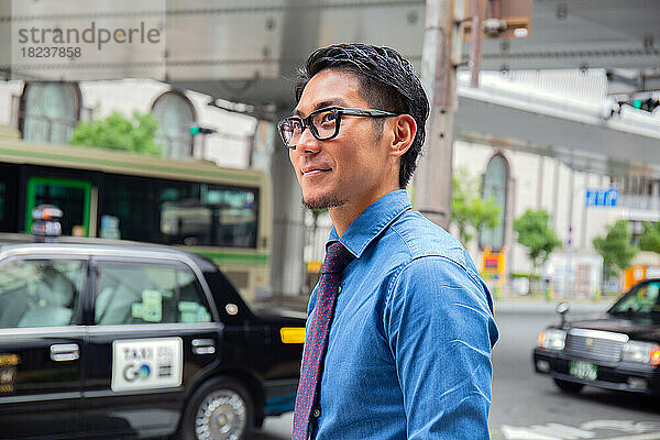 Ein junger Geschäftsmann in der Stadt  unterwegs  ein Mann in blauem Hemd und Krawatte  hinter ihm ein Taxi.