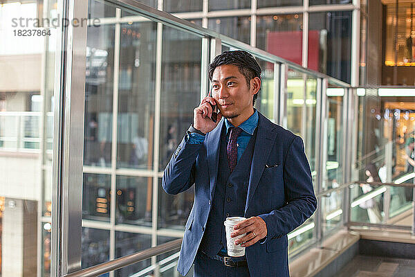 Ein junger Geschäftsmann im blauen Anzug ist in der Innenstadt unterwegs und spricht auf seinem Mobiltelefon.