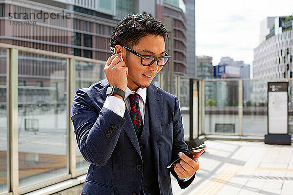 Ein junger Geschäftsmann in der Stadt  unterwegs  draußen ein Mann im Anzug  der ein Handy und sein Ohr hält und Ohrhörer benutzt.