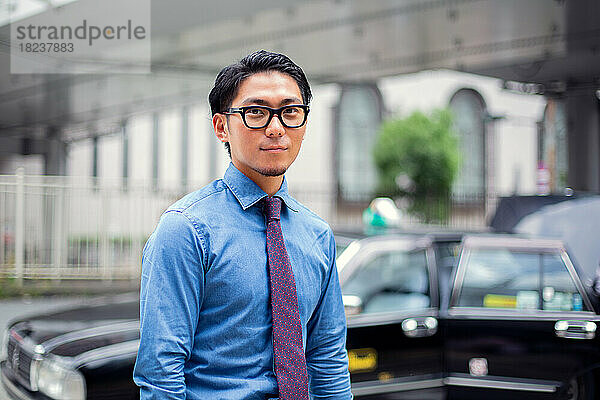 Ein junger Geschäftsmann in der Stadt  unterwegs  ein Mann mit Brille  Hemd und Krawatte  hinter ihm ein Taxi.