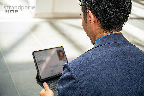 Ein junger Geschäftsmann im blauen Anzug ist in der Innenstadt unterwegs und sitzt auf einer Bank und nutzt ein digitales Tablet mit Bildschirm.
