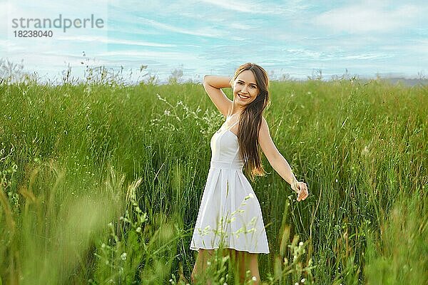 Lächelnde junge Frau im weißen Sommerkleid  die sich auf dem Feld frei fühlt