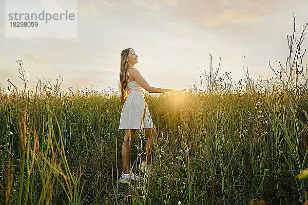Nette junge Frau im Sommerkleid hält Sonne im Feld während des Sonnenuntergangs