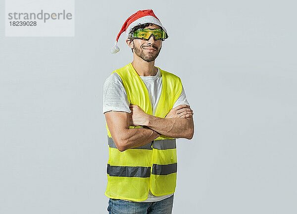 Porträt eines lächelnden Ingenieurs mit Weihnachtsmütze  Porträt eines Ingenieurs mit Weste und Weihnachtsmütze. Porträt eines fröhlichen Ingenieurs in Weste und Weihnachtsmütze mit verschränkten Armen