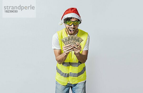 Builder Ingenieur in Weihnachtsmütze mit glücklichen Ausdruck hält Dollar isoliert. Konzept der Ingenieur mit Geld in der Ferienzeit  Ingenieur in Weihnachtsmütze hält Geld lächelnd in die Kamera