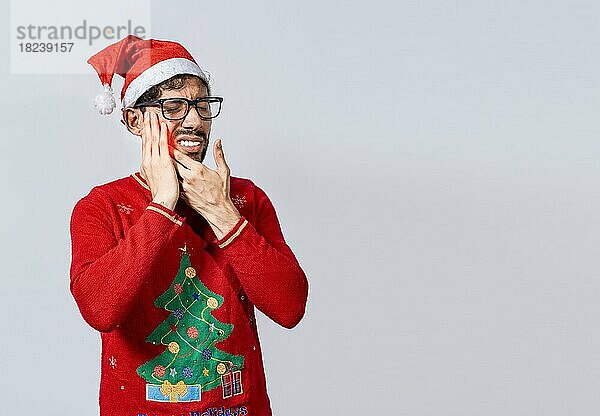 Mann im Weihnachtspulli mit Zahnschmerzen  Junger Mann in Weihnachtsmütze mit Zahnschmerzen isoliert  Mann mit Weihnachtsmütze in Schmerzen berührt seinen Zahn. Weihnachten Zahnschmerzen Konzept