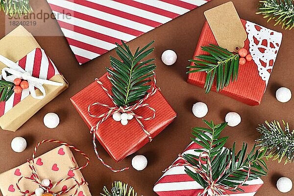 Draufsicht auf schöne rot  weiß und natürlich braun dekoriert Weihnachtsgeschenk-Boxen mit Bändern und Tannenzweigen auf braunem Hintergrund