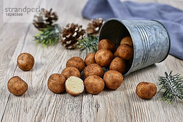 Traditionelle deutsche Weihnachtsbonbons  genannt Marzipankartoffeln. Runde  kugelförmige  mit Zimt und Kakaopulver bestreute Mandelpastetchen  die aus einem Eisenbecher auf Holzuntergrund quellen