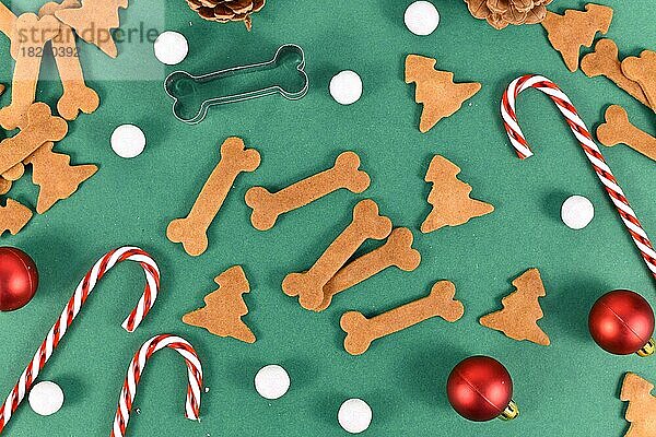 Hausgemachte gebackene Hundekekse in Form von Knochen und Weihnachtsbaum auf festlichen grünen Hintergrund mit Zuckerstangen und Baumkugeln verziert