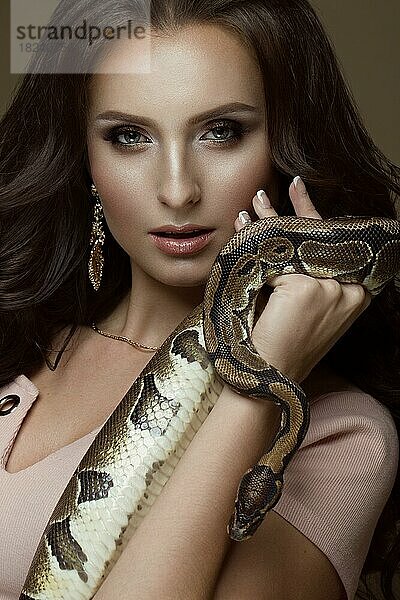 Schönes Mädchen brunette Modell  perfekte Locken und Abendmode Make-up mit einer Schlange in ihren Händen. Schönheit Gesicht. Bild im Studio auf einem schwarzen Hintergrund genommen