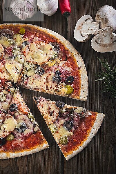 Aufgeschnittene leckere frische Pizza mit Pilzen und Wurst auf einem hölzernen Hintergrund. Ansicht von oben. Nahaufnahme