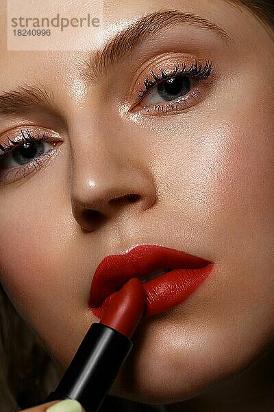 Schönes Mädchen mit roten Lippen und klassischen Make-up mit Lippenstift in der Hand. Schönes Gesicht. Foto im Studio aufgenommen