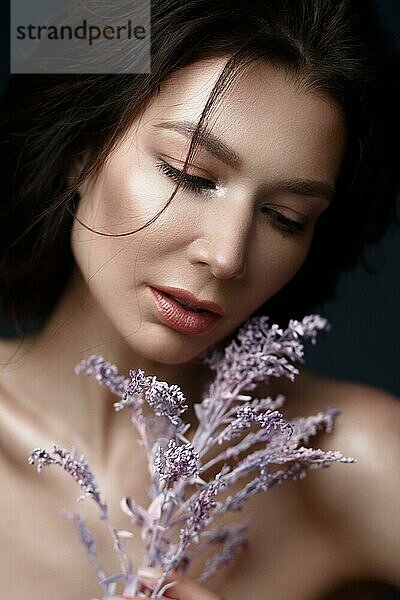 Schöne Frau mit einem leichten natürlichen Make-up und perfekter Haut mit Blumen in der Hand. Schönes Gesicht. Bild im Studio auf einem schwarzen Hintergrund aufgenommen