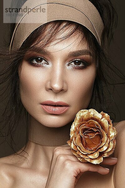 Schöne Frau mit einem hellen Make-up und perfekte Haut mit goldenen Blumen in der Hand. Schönes Gesicht. Bild im Studio auf einem schwarzen Hintergrund aufgenommen