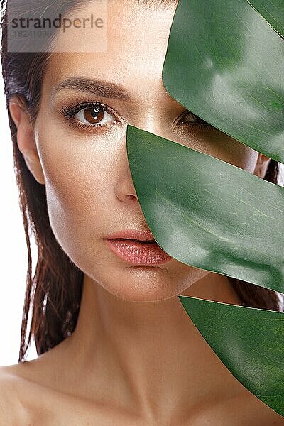 Schöne frische Mädchen mit perfekter Haut  natürliches Make-up und grüne Blätter. Schönes Gesicht. Foto im Studio aufgenommen