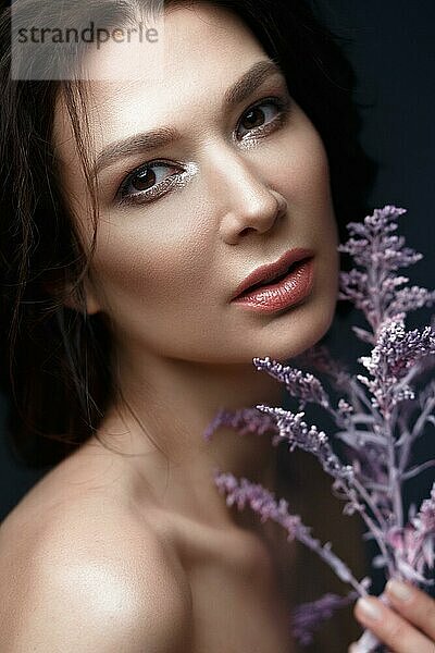 Schöne Frau mit einem leichten natürlichen Make-up und perfekter Haut mit Blumen in der Hand. Schönes Gesicht. Bild im Studio auf einem schwarzen Hintergrund aufgenommen