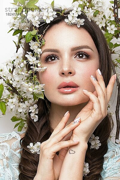 Schönes brünettes Mädchen in blauem Kleid mit einem sanften romantischen Make-up  rosa Lippen und Blumen. Die Schönheit des Gesichts. Porträtaufnahme im Studio