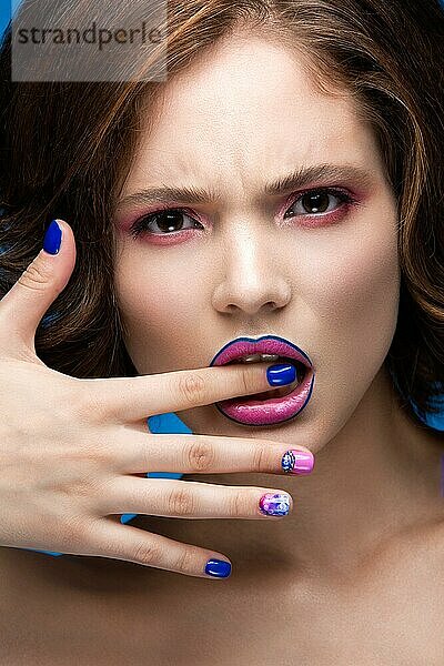 Schönes Modell Mädchen mit hellen Make-up und farbigen Nagellack. Schönes Gesicht. Kurze bunte Nägel. Bild im Studio auf einem blauen Hintergrund genommen