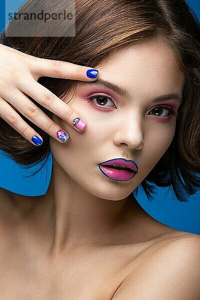 Schönes Modell Mädchen mit hellen Make-up und farbigen Nagellack. Schönes Gesicht. Kurze bunte Nägel. Bild im Studio auf einem blauen Hintergrund genommen