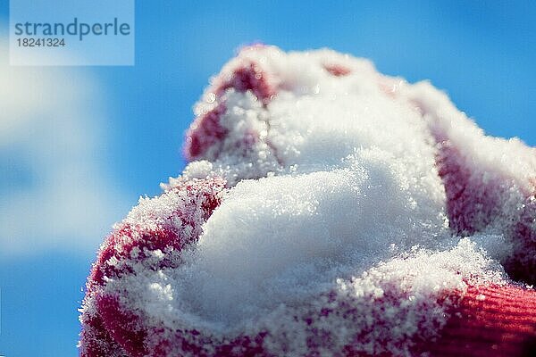 Herz aus Schnee auf den gestrickten roten Handschuhen