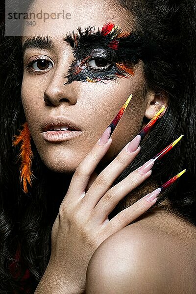 Schönes Mädchen im Bild des Phoenix-Vogels mit kreativem Make-up und langen Nägeln. Maniküre Design. Die Schönheit des Gesichts. Fotos im Studio geschossen