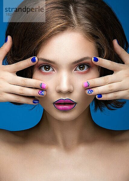 Schönes Modell Mädchen mit hellen Make-up und farbigen Nagellack. Schönes Gesicht. Kurze bunte Nägel. Bild im Studio auf einem blauen Hintergrund genommen