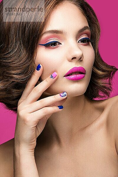 Schönes Modell Mädchen mit hellen Make-up und farbigen Nagellack. Schönes Gesicht. Kurze bunte Nägel. Bild im Studio auf einem rosa Hintergrund genommen