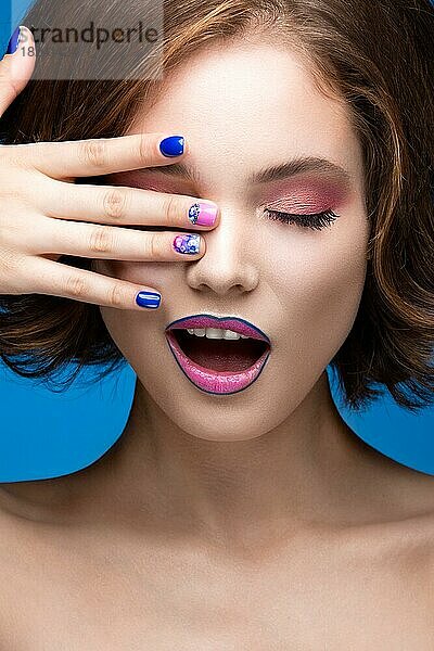 Schönes Modell Mädchen mit hellen Make-up und farbigen Nagellack. Schönes Gesicht. Kurze bunte Nägel. Bild im Studio auf einem blauen Hintergrund genommen