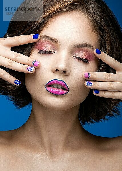 Schönes Modell Mädchen mit hellen Make-up und farbigen Nagellack. Schönes Gesicht. Kurze bunte Nägel. Bild im Studio auf einem blauen Hintergrund genommen