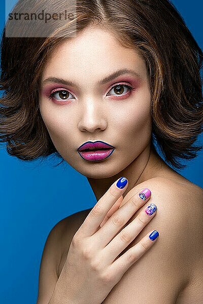 Schönes Modell Mädchen mit hellen Make-up und farbigen Nagellack. Schönes Gesicht. Kurze bunte Nägel. Bild im Studio auf einem blauen Hintergrund genommen