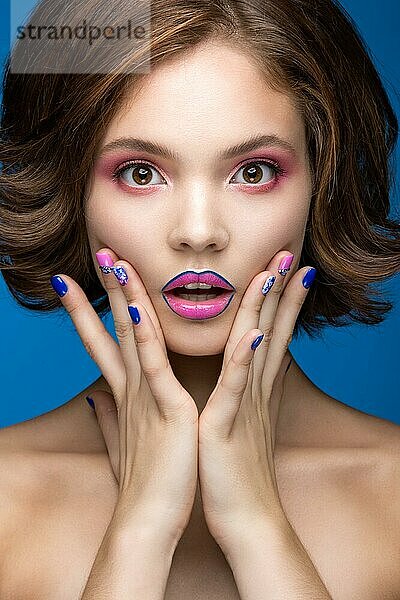 Schönes Modell Mädchen mit hellen Make-up und farbigen Nagellack. Schönes Gesicht. Kurze bunte Nägel. Bild im Studio auf einem blauen Hintergrund genommen